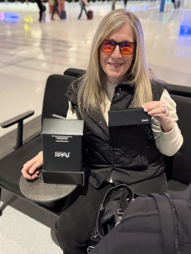 Rachel Friem holding a FlyKitt travel kit at Pittsburgh International Airport while wearing glasses before a flight