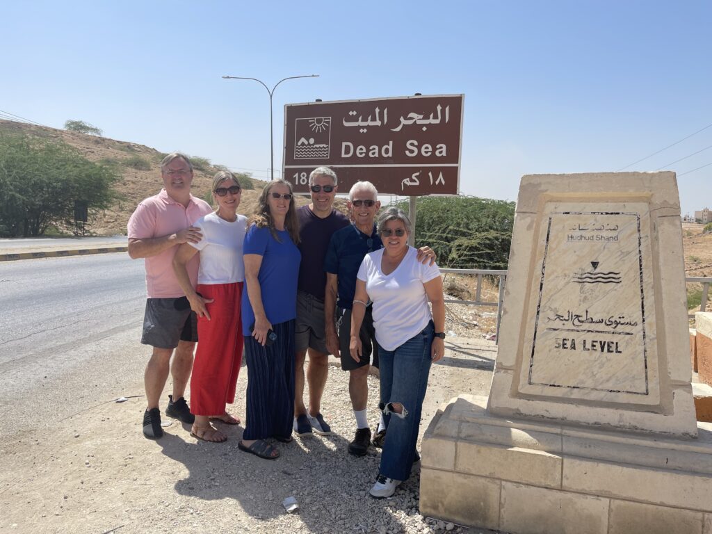Rachel standing with her father, stepmother, brother, and sister-in-law in front of the Dead Sea sign in Jordan, capturing a multigenerational family travel moment in a desert landscape.