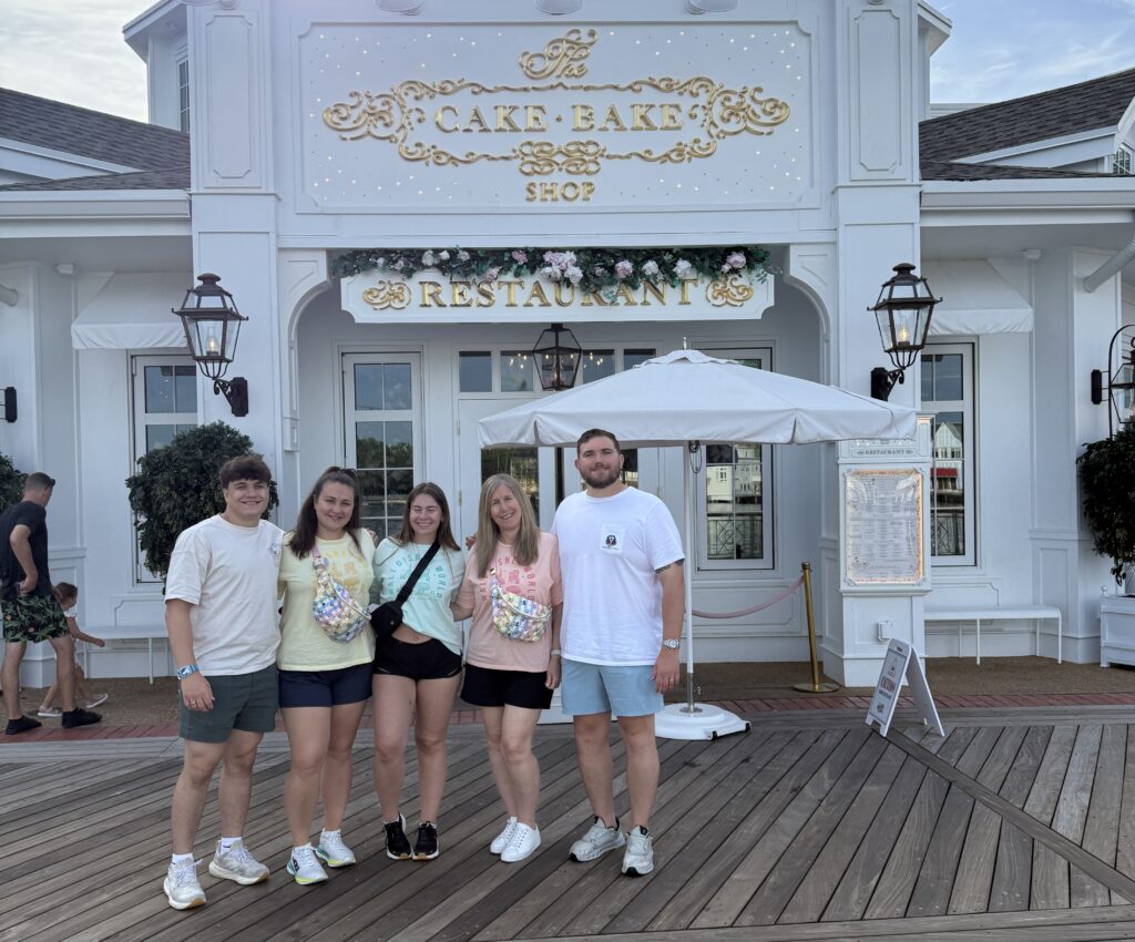 Image of Rachel Mayer frame GENXTRAVELMOM with her two sons daughter-in-law and son's girlfriend in front of the cake bake shop on the boardwalk enjoying food wearing stony clover bags and Paul green shoes